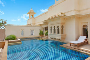 Private pool with blue mosaic tiles at Udaivilas, a luxury hotel in India, showcasing traditional architecture under a clear sky.