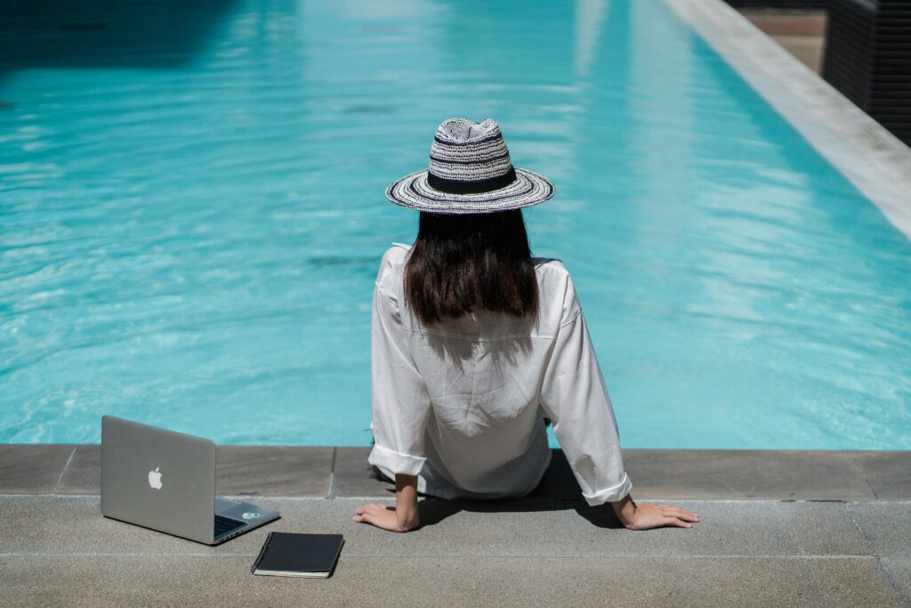 Faceless female freelancer resting-at hotel poolside after work on laptop